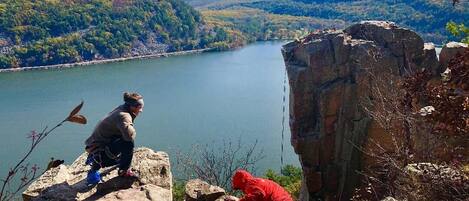 A person in a red jacket climbing a rocky cliff overlooking a lake.