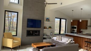 Un salon moderne avec un canapé, un fauteuil jaune, une table basse, un téléviseur à écran plat fixé au mur et une cheminée.
