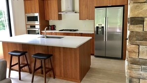 Une cuisine moderne avec des armoires en bois, des appareils en acier inoxydable, un grand îlot central doté de tabourets et un mur d’accent en pierre.