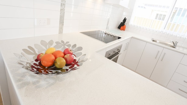 A kitchen with white cabinets, a stainless steel sink, and a fruit bowl on the counter.