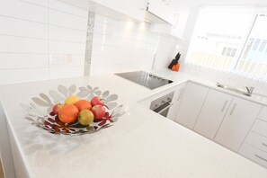 Una cocina con armarios blancos, un lavamanos de acero inoxidable y un bol de frutas en la encimera.