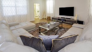 A modern living room with a white sofa, a coffee table, and a flat-screen TV. - Jr Champions by VillaDirect (Davenport)