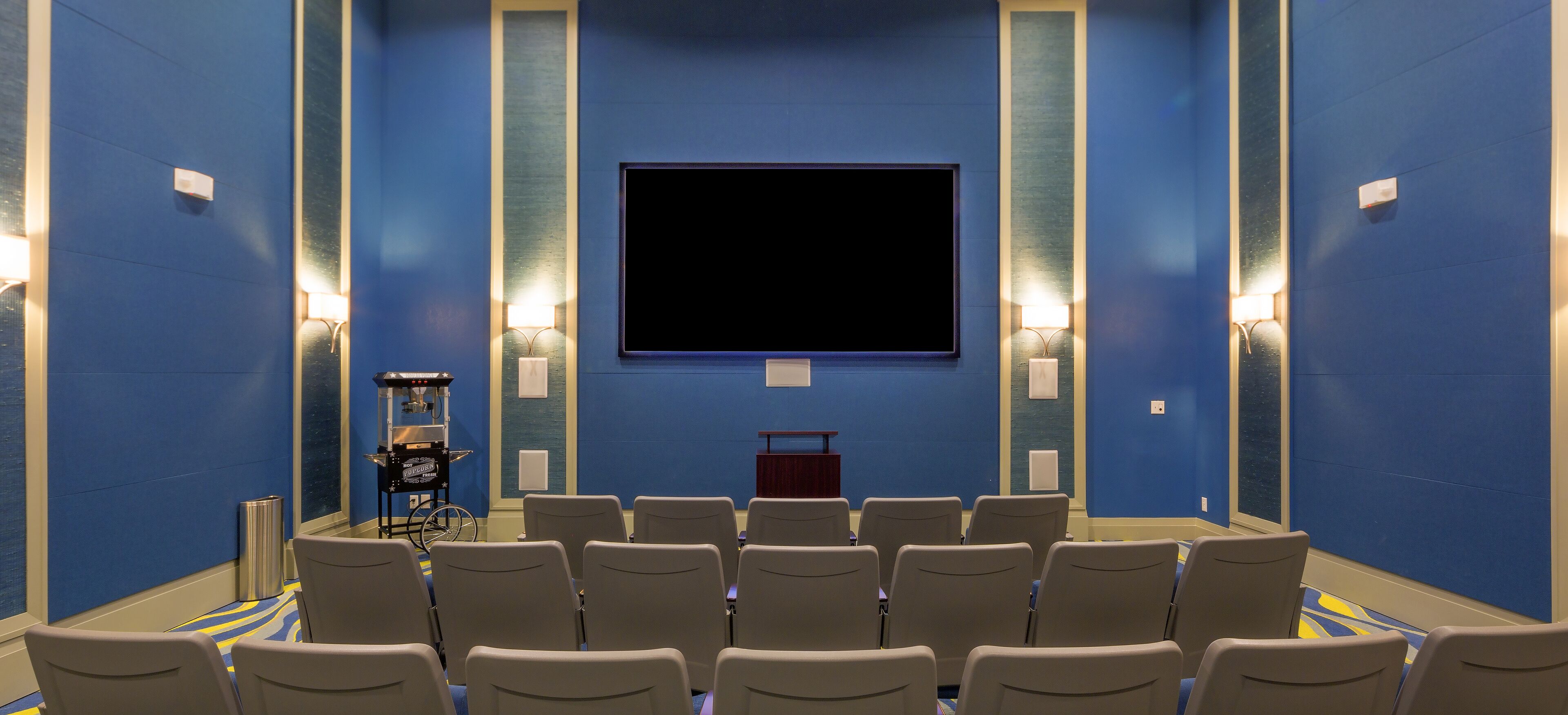 A theater with rows of seats, a large screen, and wall-mounted lighting.