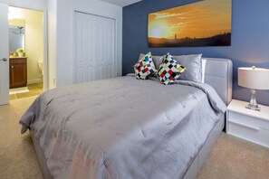 Ein Schlafzimmer mit einem Bett, einem Nachttisch, einer Lampe, einem Gemälde und einer Tür zum Badezimmer.