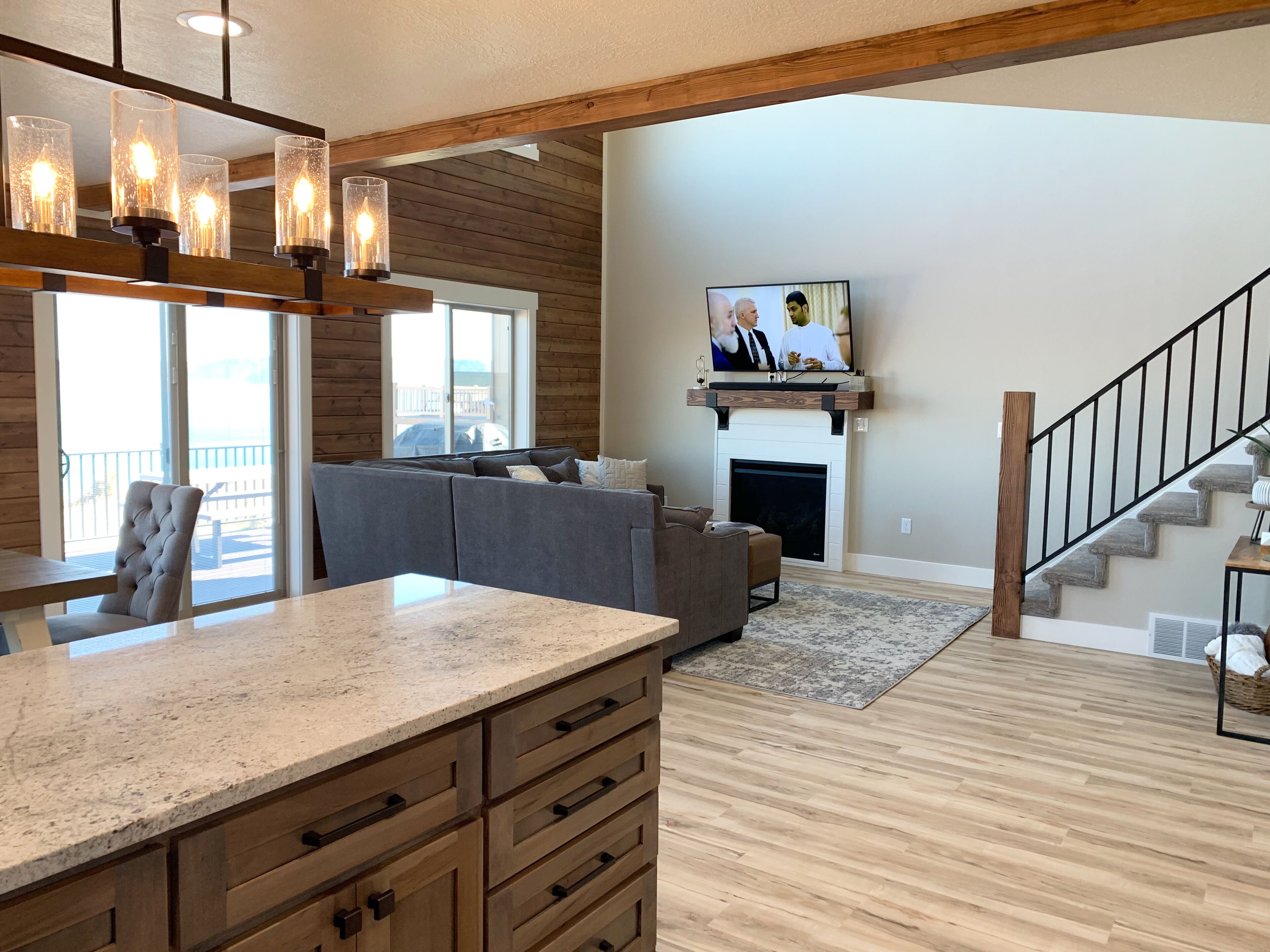 A spacious living room with a fireplace, a television mounted above it, and a staircase leading to an upper level.