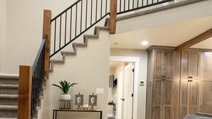 Ein geräumiger Wohnbereich mit Treppe, einem grauen Sofa, einem gemusterten Teppich und Holzschränken.