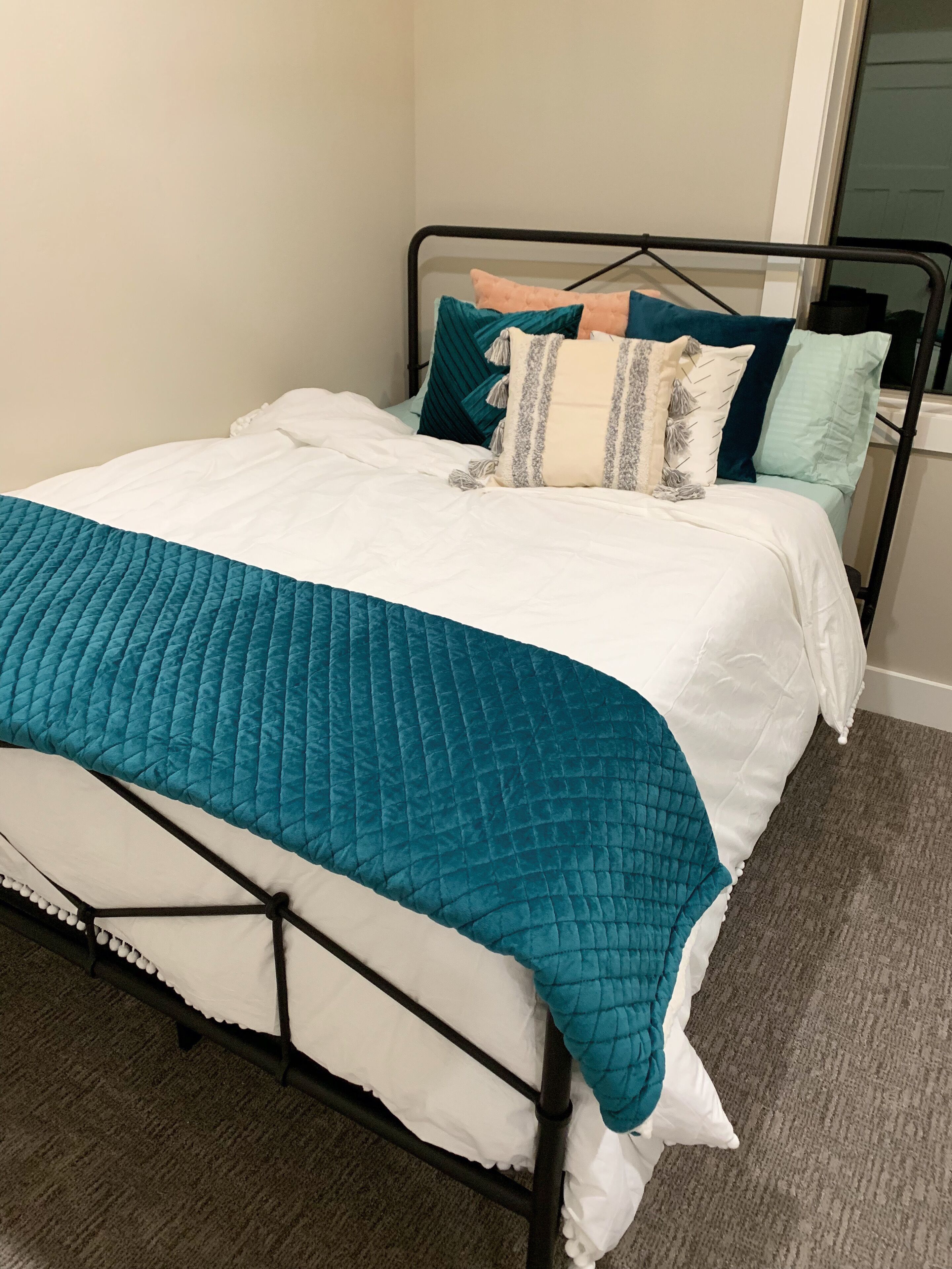 A bed with a teal quilt, white bedding, and multiple pillows in various colors and patterns.