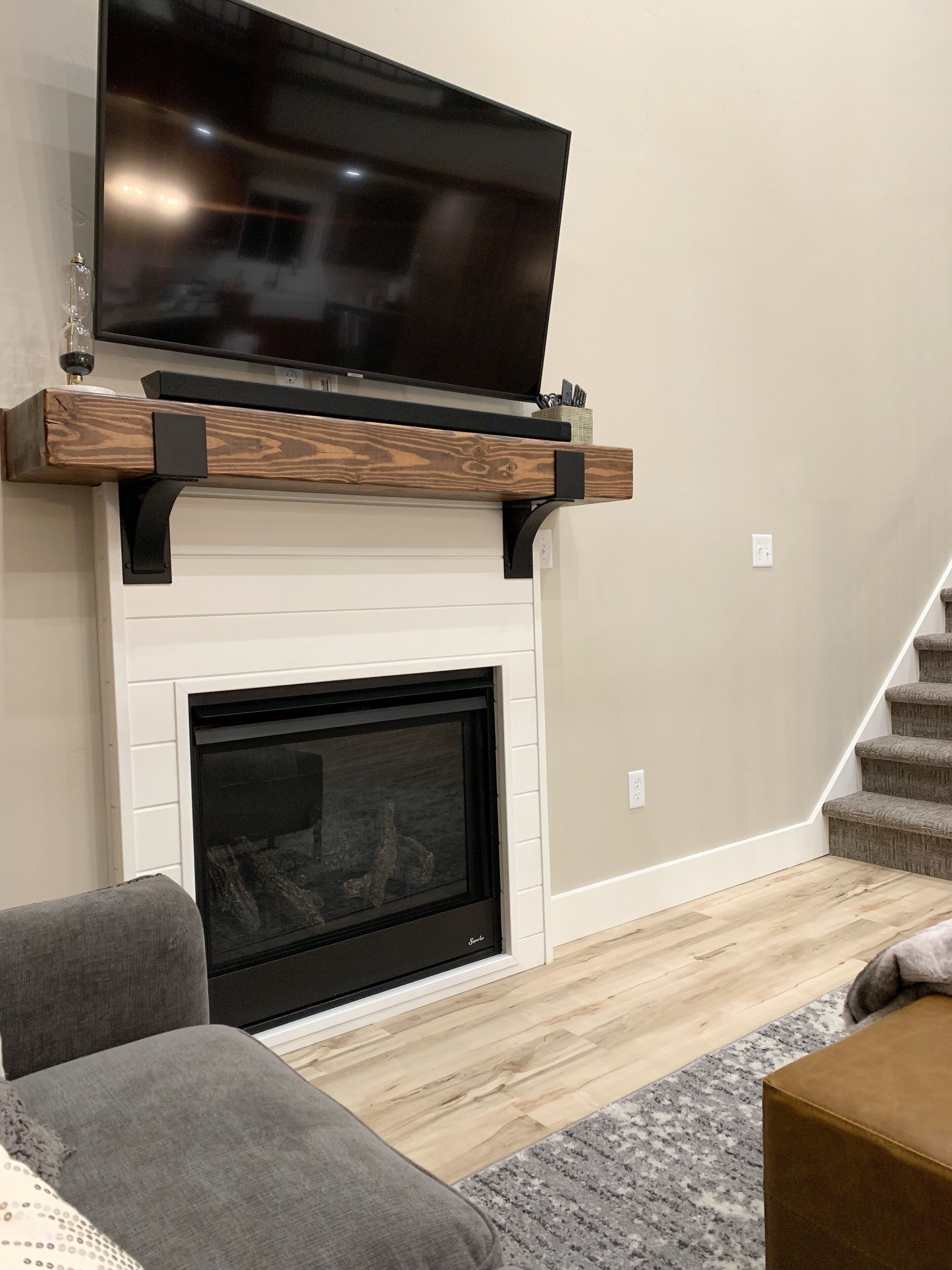 A modern living room with a flat-screen TV mounted on a wooden shelf above a white fireplace.