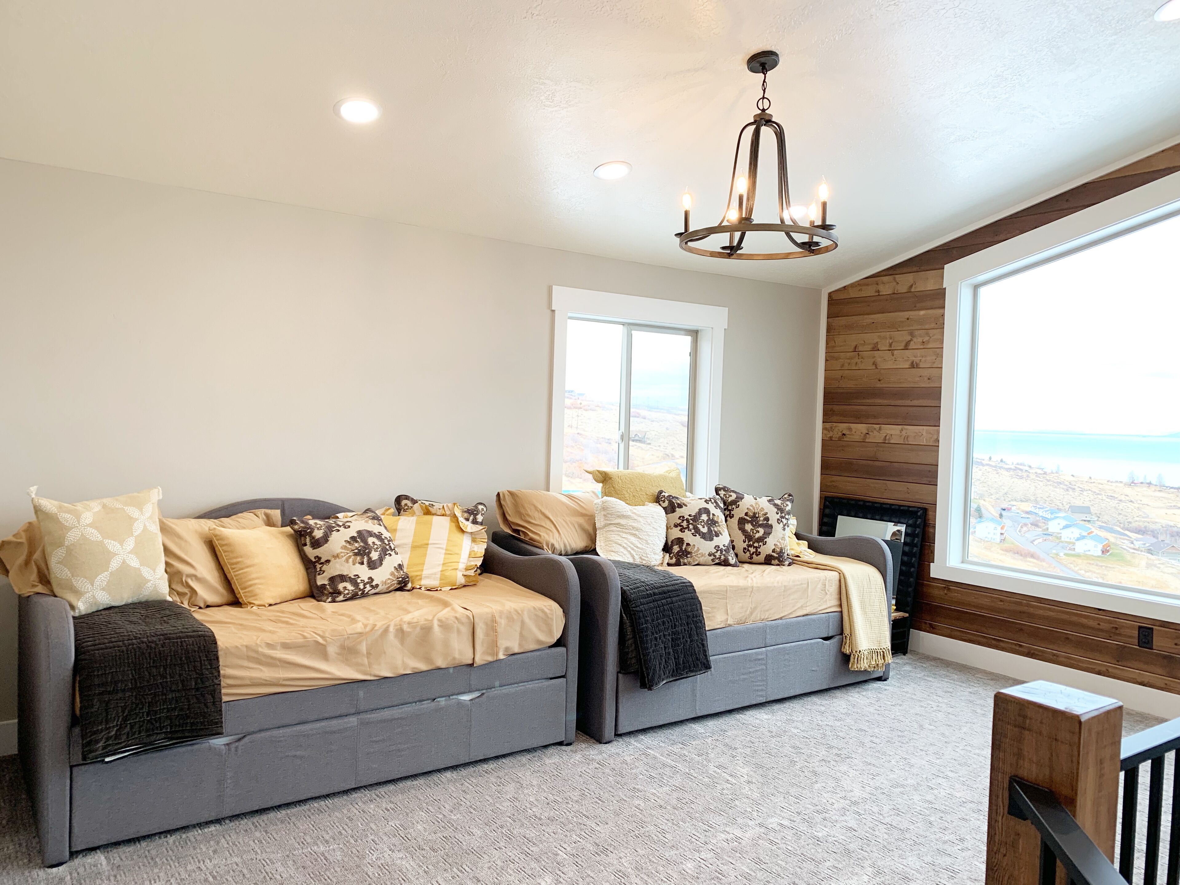 A spacious living room with a grey sofa set, a chandelier, and a large window offering a view of a distant landscape.