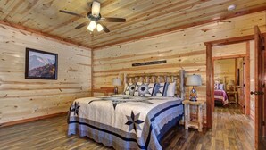 A wooden cabin bedroom with a bed, a ceiling fan, a nightstand, and a door leading to another room. - Private Heated Indoor Pool, Mountain View, Hot Tub, Pigeon Forge Cabin, Pool Table, Theater Room (Sevierville)