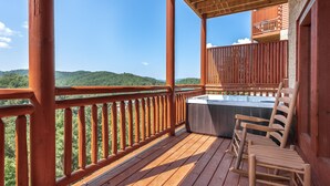A wooden deck with a hot tub and chairs, overlooking a forested landscape. - Private Heated Indoor Pool, Mountain View, Hot Tub, Pigeon Forge Cabin, Pool Table, Theater Room (Sevierville)