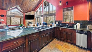 A spacious kitchen with dark wooden cabinets, a granite countertop, and a stone fireplace.