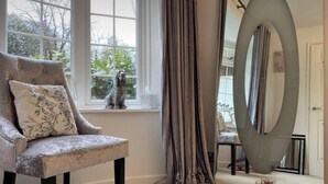 Una habitación con un sillón capitoné, un espejo ovalado grande y vistas al verdor exterior.