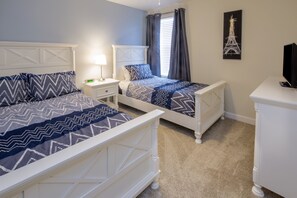 A bedroom with two beds, a nightstand with a lamp, a dresser, and a wall-mounted TV.