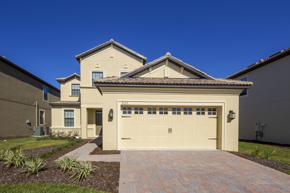 A two-story house with a beige exterior, a garage, and a well-maintained front yard with a brick pathway.