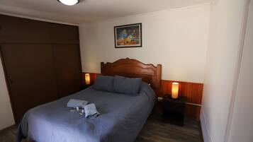 A neatly made bed with a wooden headboard, a bedside table with a lamp, and a painting on the wall.