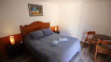 Un dormitorio con una cama grande, cabecera de madera, dos mesitas de noche con lámparas, una pequeña mesa redonda con sillas y un cuadro en la pared.