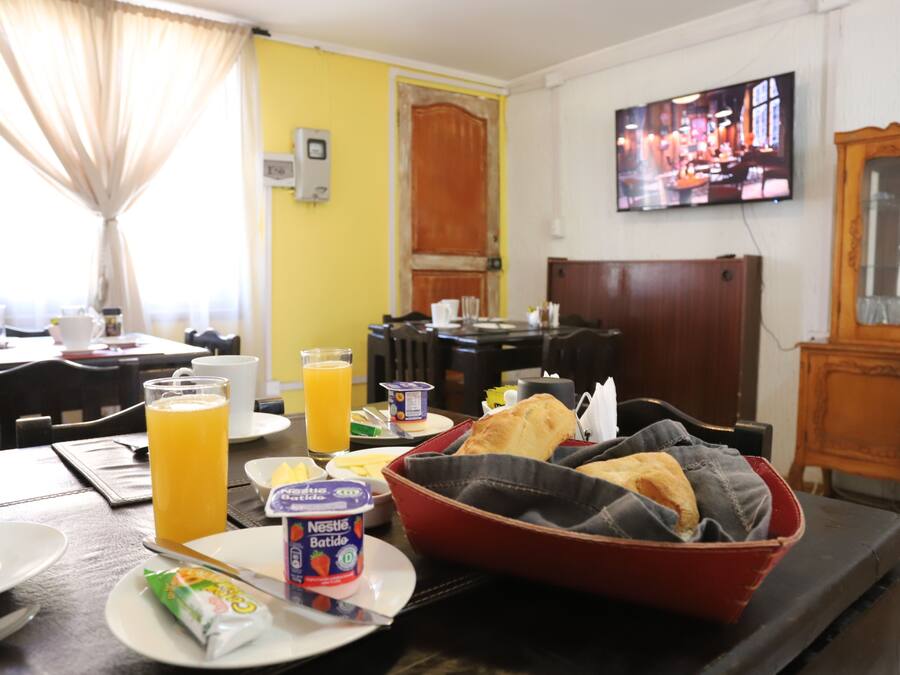 Een ontbijtopstelling met een rode kom met brood, een bord met een drankje en een snack, en een ontbijttafel met stoelen.