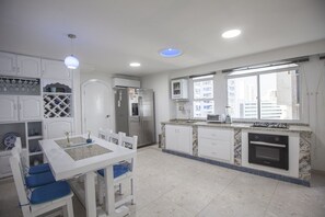 A modern kitchen with white cabinetry, a dining table with blue chairs, a built-in oven, and a window providing a view of the city.
