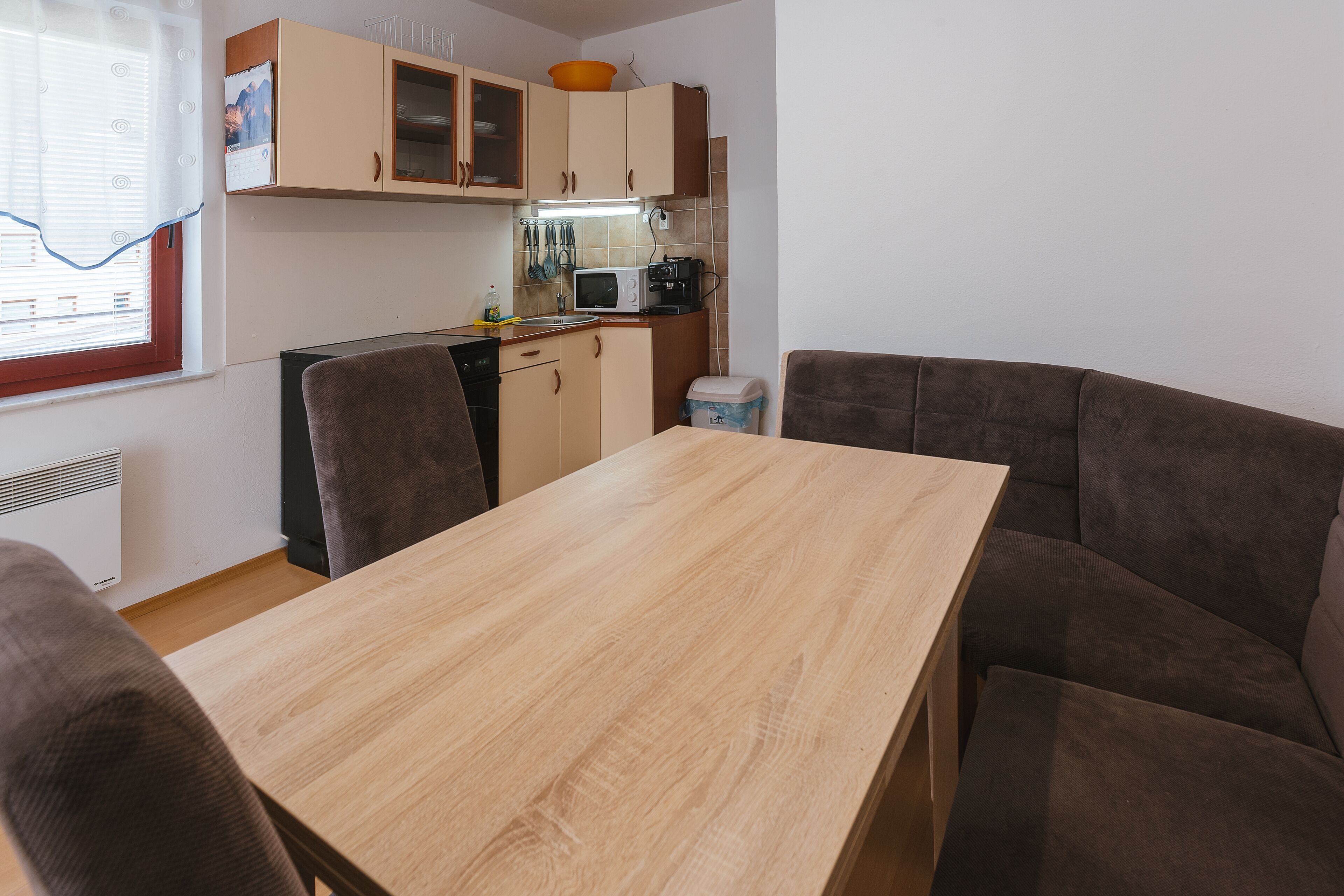 A compact kitchen with a microwave, toaster, and cabinets. There is a dining table with four chairs and a window with blinds.
