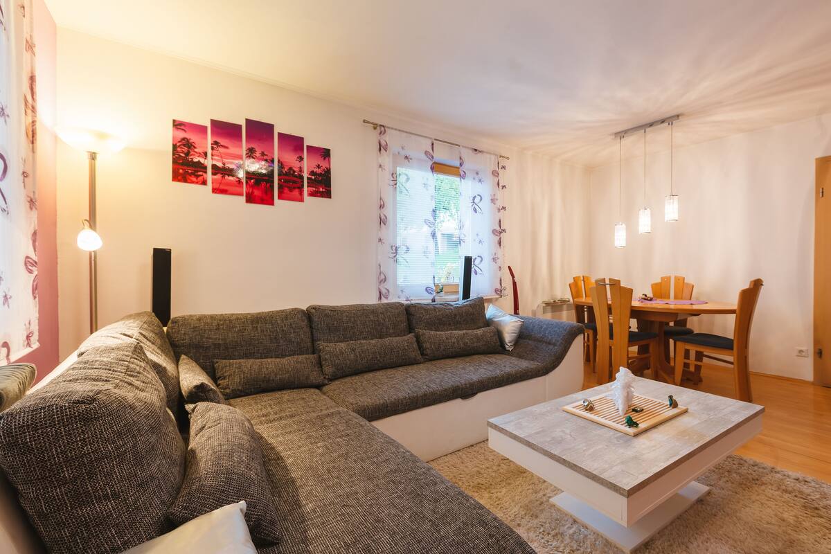 Una sala de estar con un sofá modular, una mesa de comedor con sillas y una mesa de centro.