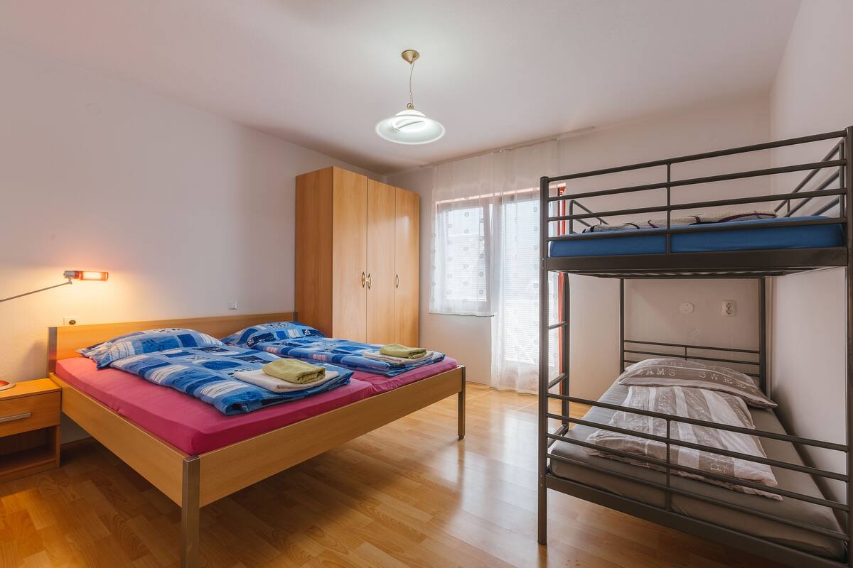 Un dormitorio con una cama litera, un armario de madera, un escritorio con lámpara y una ventana con cortinas.