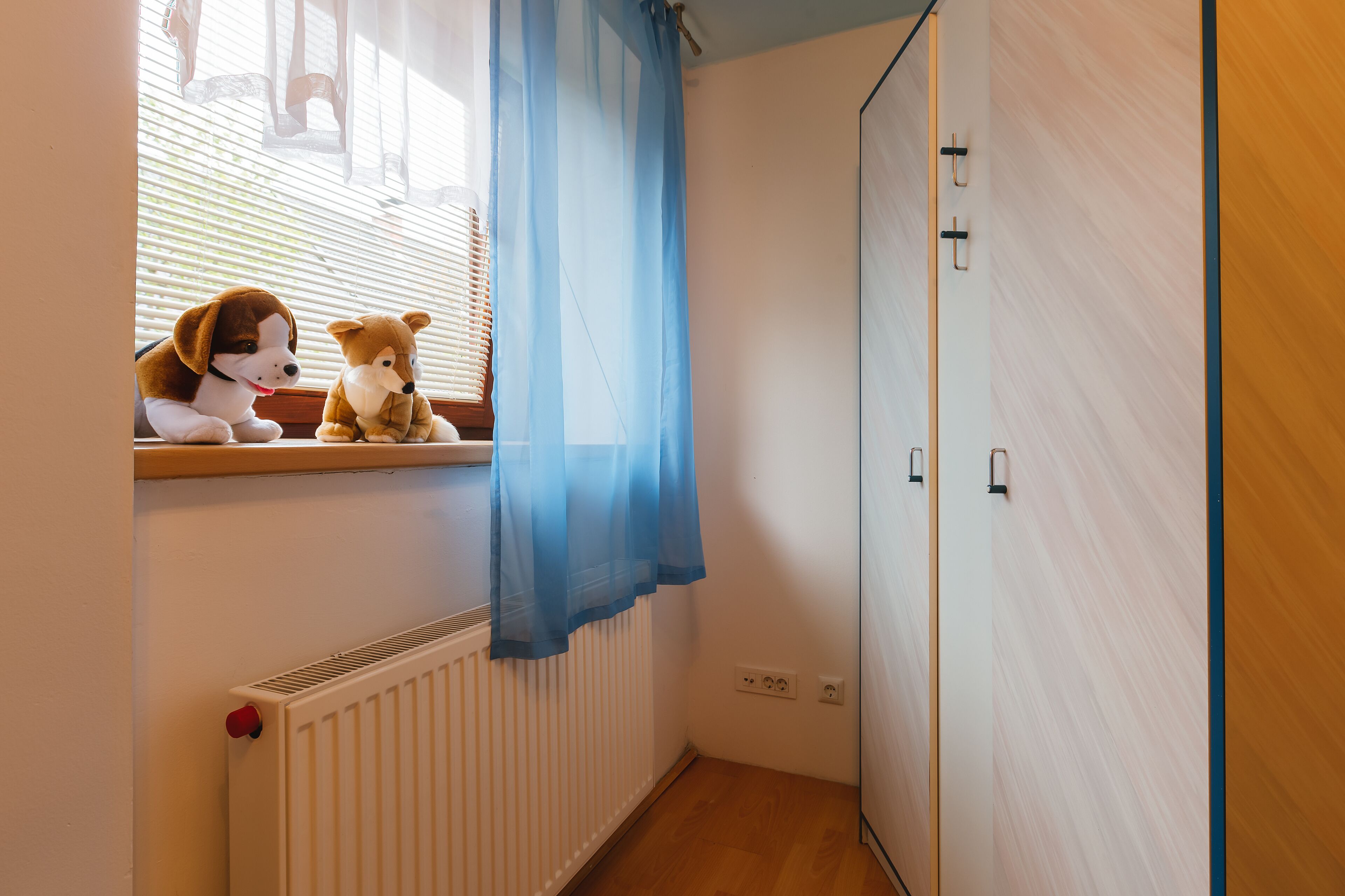 A room with a window, a radiator, a wooden floor, and a wardrobe.