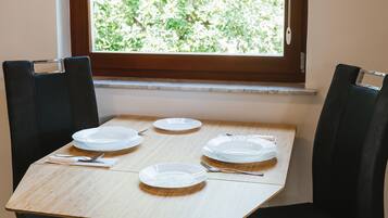 Une table à manger avec quatre assiettes blanches, des couverts et une serviette. La table est placée devant une fenêtre donnant sur un paysage verdoyant.