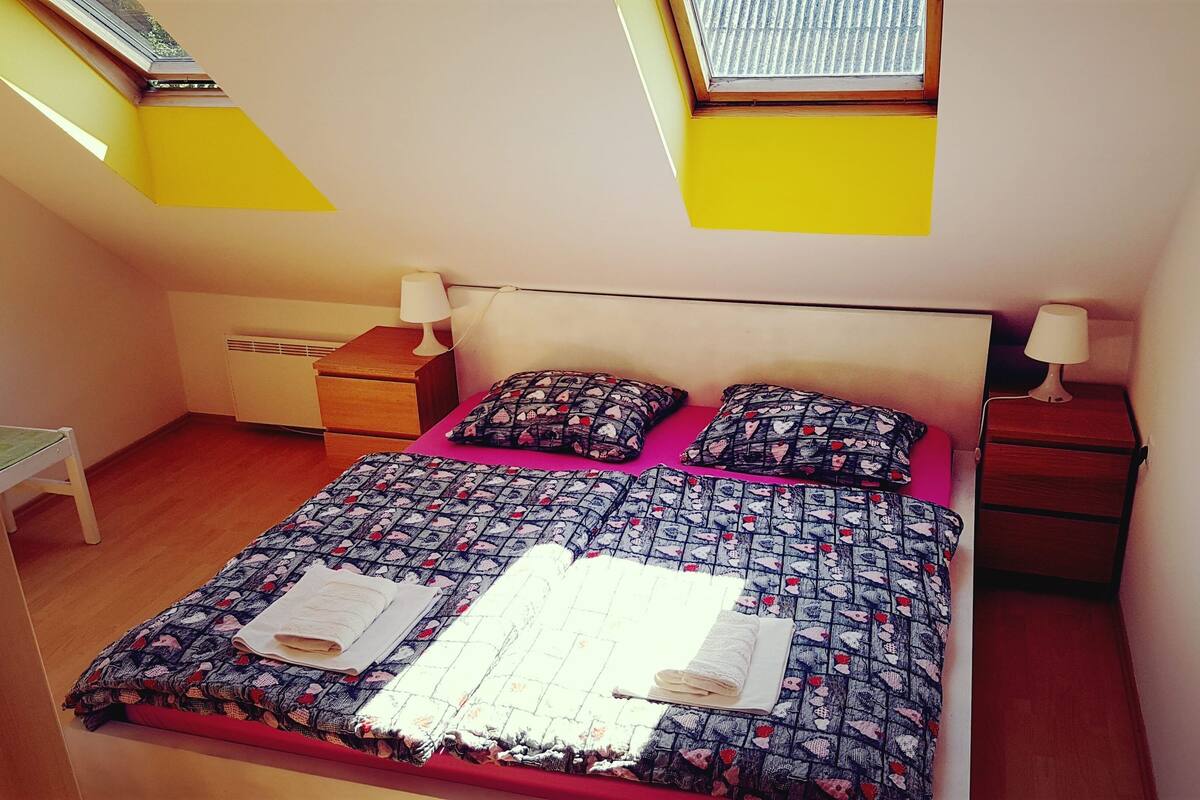 Un dormitorio con una cama, dos mesitas de noche, una silla y un tragaluz.