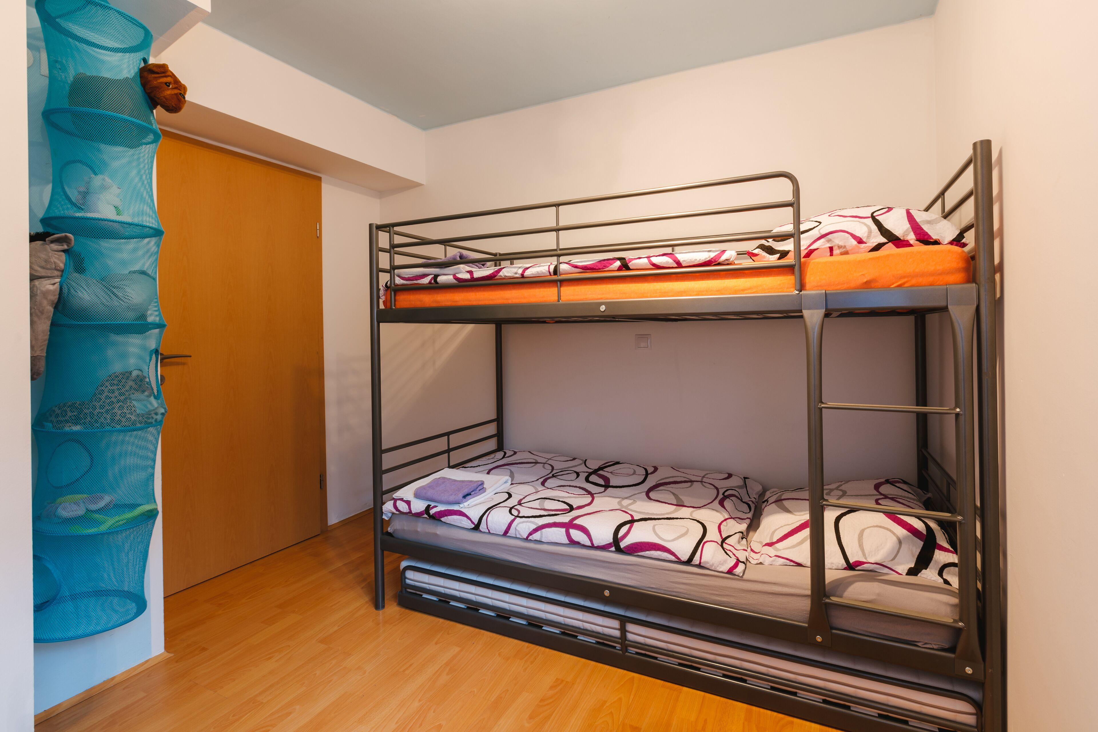 Ein Etagenbett mit gemustertem Bettbezug und einer Stauraumeinheit mit Netzkörben.