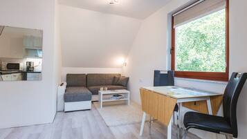 Un espacio habitable compacto con kitchenette, un sofá, una mesa de comedor y una ventana con vista a la vegetación.