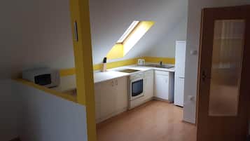 Una cucina compatta con un lucernario, mobili bianchi, un forno a microonde, un piano cottura e un frigorifero.
