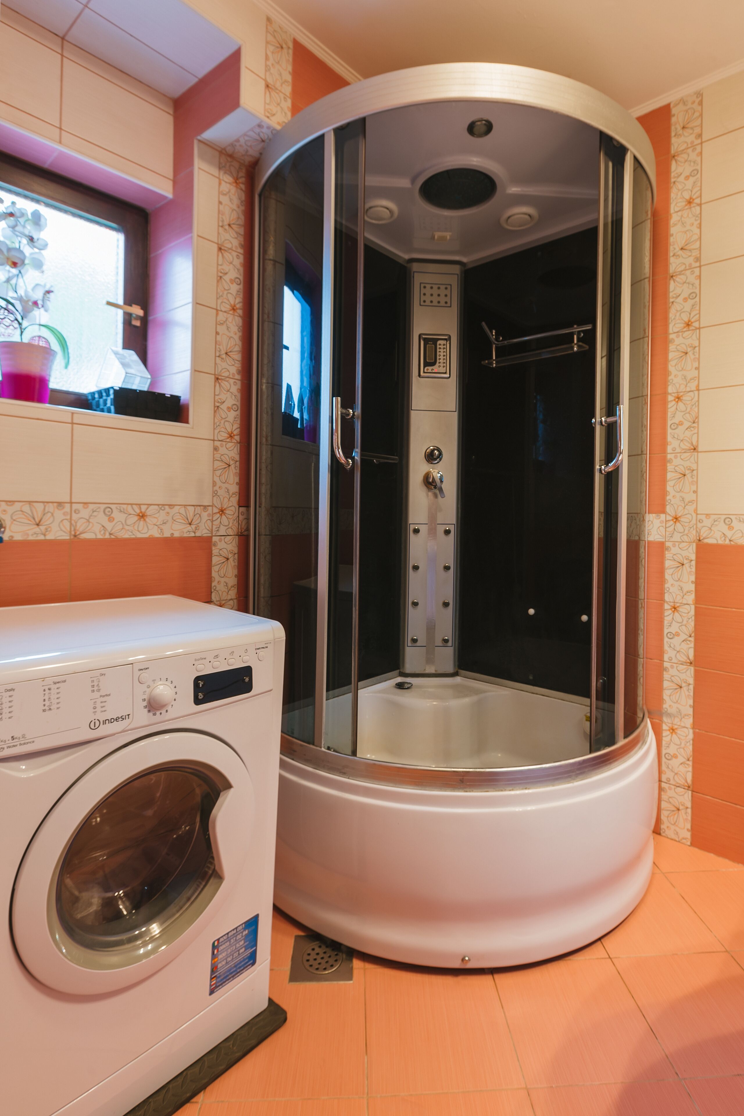 A compact bathroom with a washing machine and a glass-enclosed shower stall.