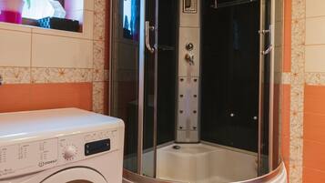 A compact bathroom with a washing machine and a glass-enclosed shower stall.