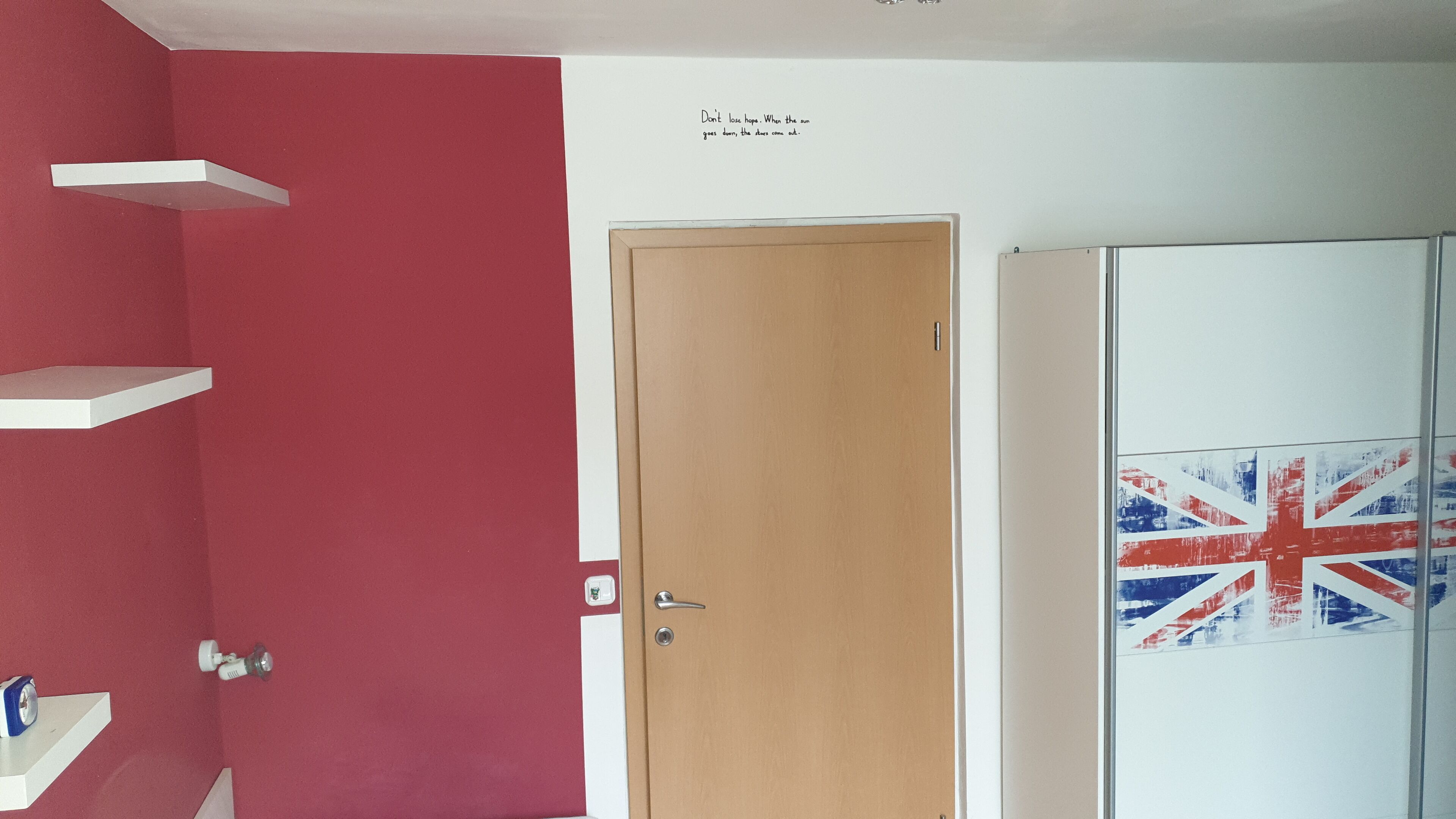 A room with a wooden door, a shelf unit, and a wall with a motivational quote.