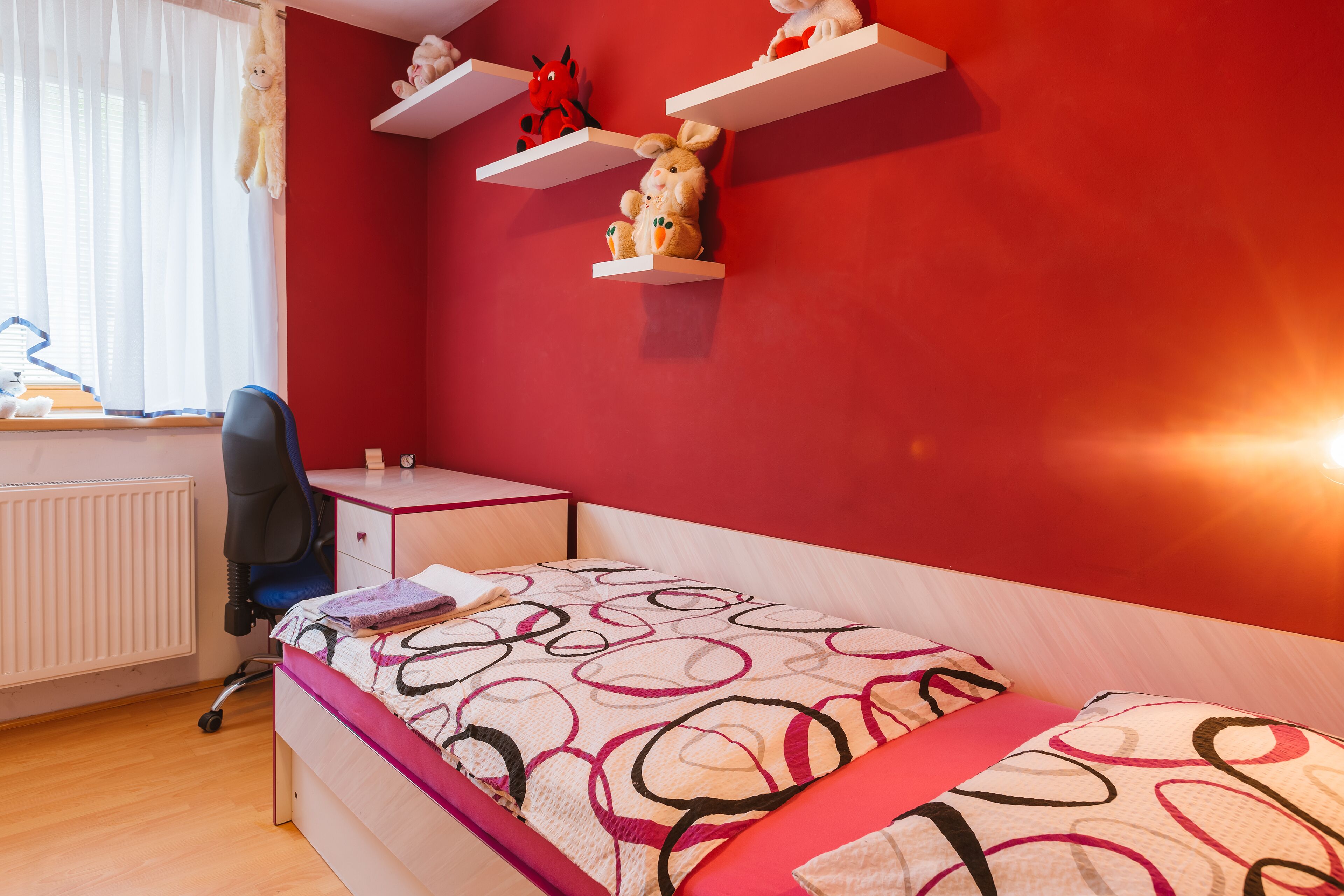 A bedroom with a bed, a desk, a chair, and shelves with stuffed toys.