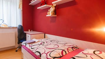 A bedroom with a bed, a desk, a chair, and shelves with stuffed toys.