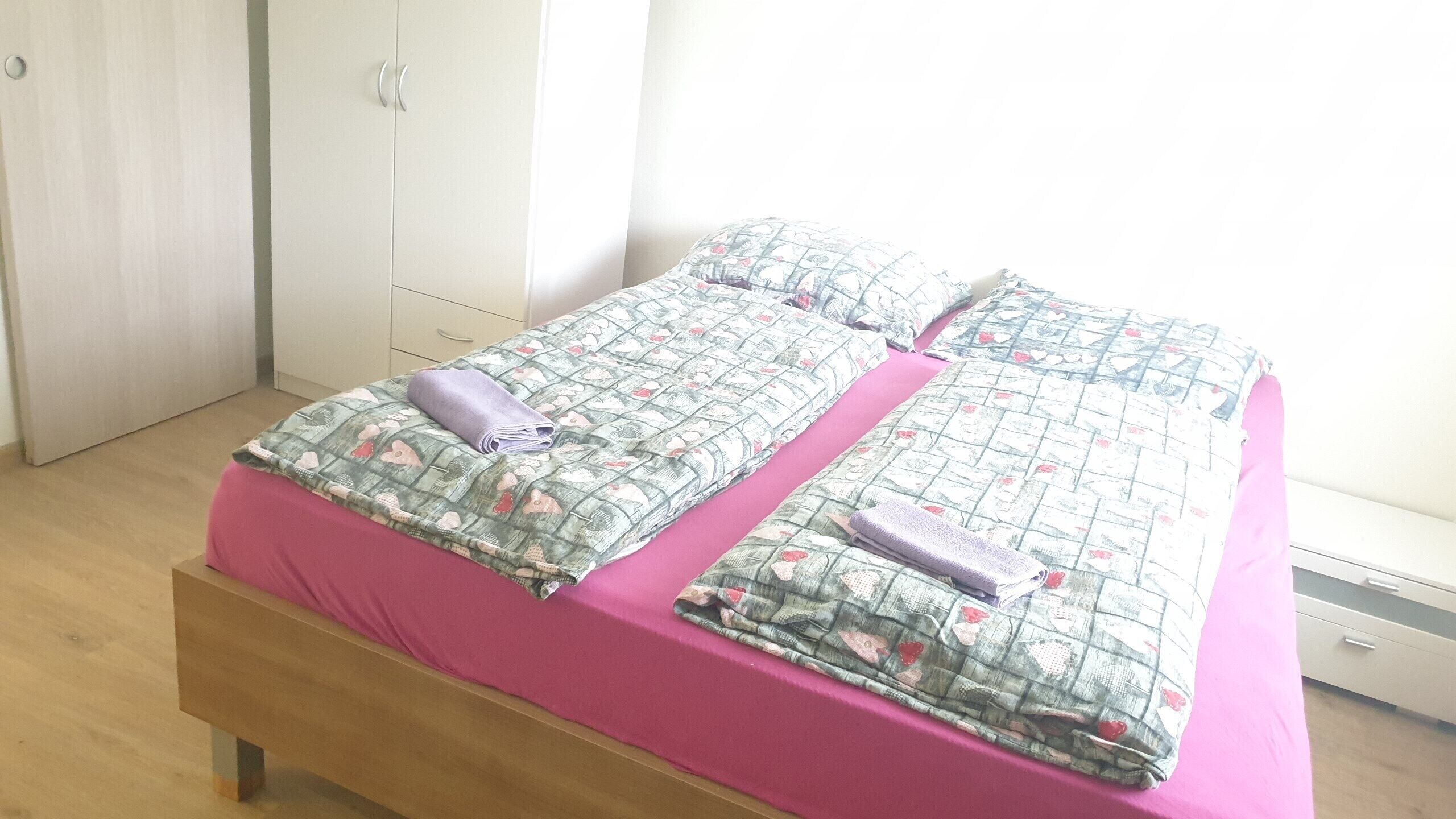 Ein Doppelbett mit floralem Bettzeug, einer rosa Tagesdecke und zwei aufgerollten Handtüchern.