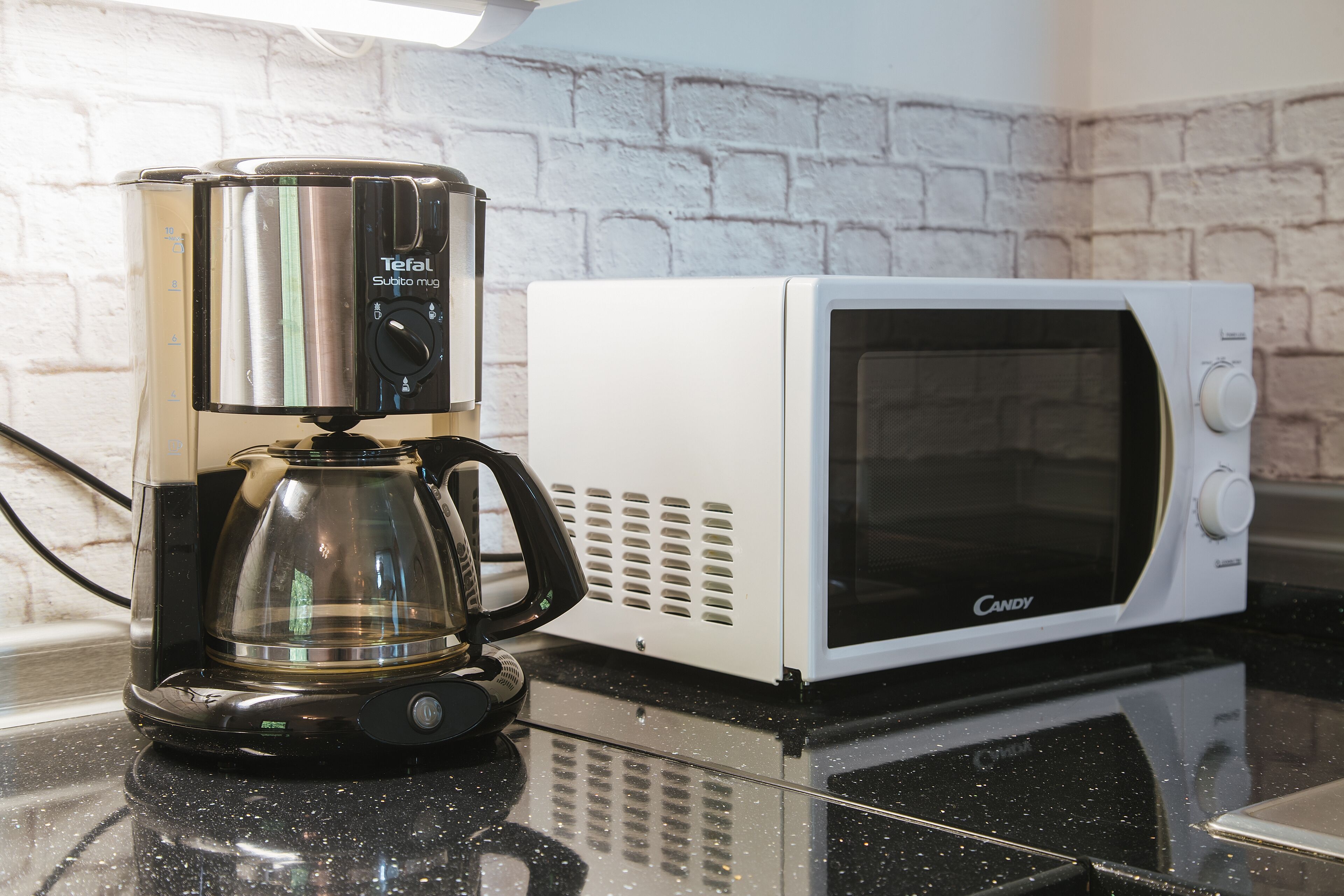 A coffee maker and a microwave on a kitchen counter with a white brick backsplash.