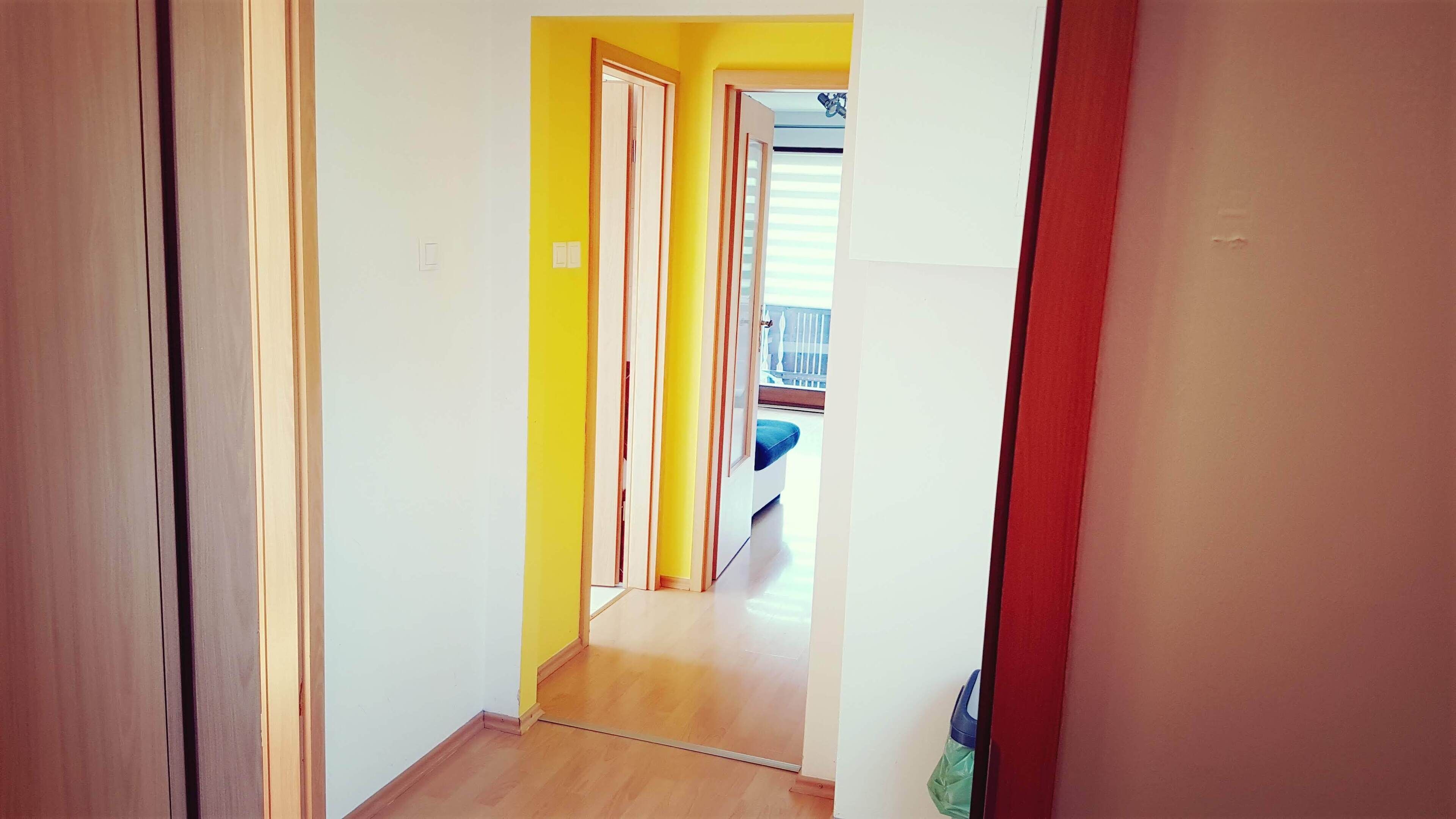 A narrow hallway with wooden flooring and yellow walls.