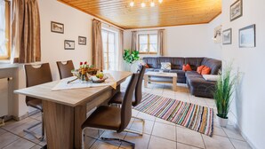 A modern living room with a wooden ceiling, a dining area with a table and chairs, and a sofa with cushions. - Apartment 54sqm, balcony, kitchen, 1 bedroom, living room, max. 2 persons (Ruhpolding)