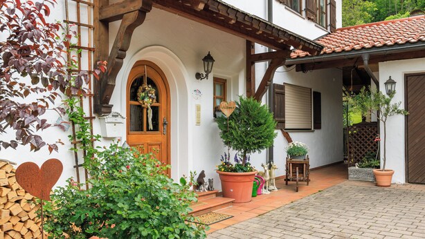 A traditional European-style house with a wooden porch, a tiled roof, and a variety of potted plants and garden decorations. - Apartment 54sqm, balcony, kitchen, 1 bedroom, living room, max. 2 persons (Ruhpolding)