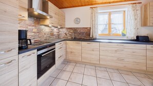 A modern kitchen with wooden cabinets, a stone backsplash, and a large window with curtains. - Apartment 54sqm, balcony, kitchen, 1 bedroom, living room, max. 2 persons (Ruhpolding)