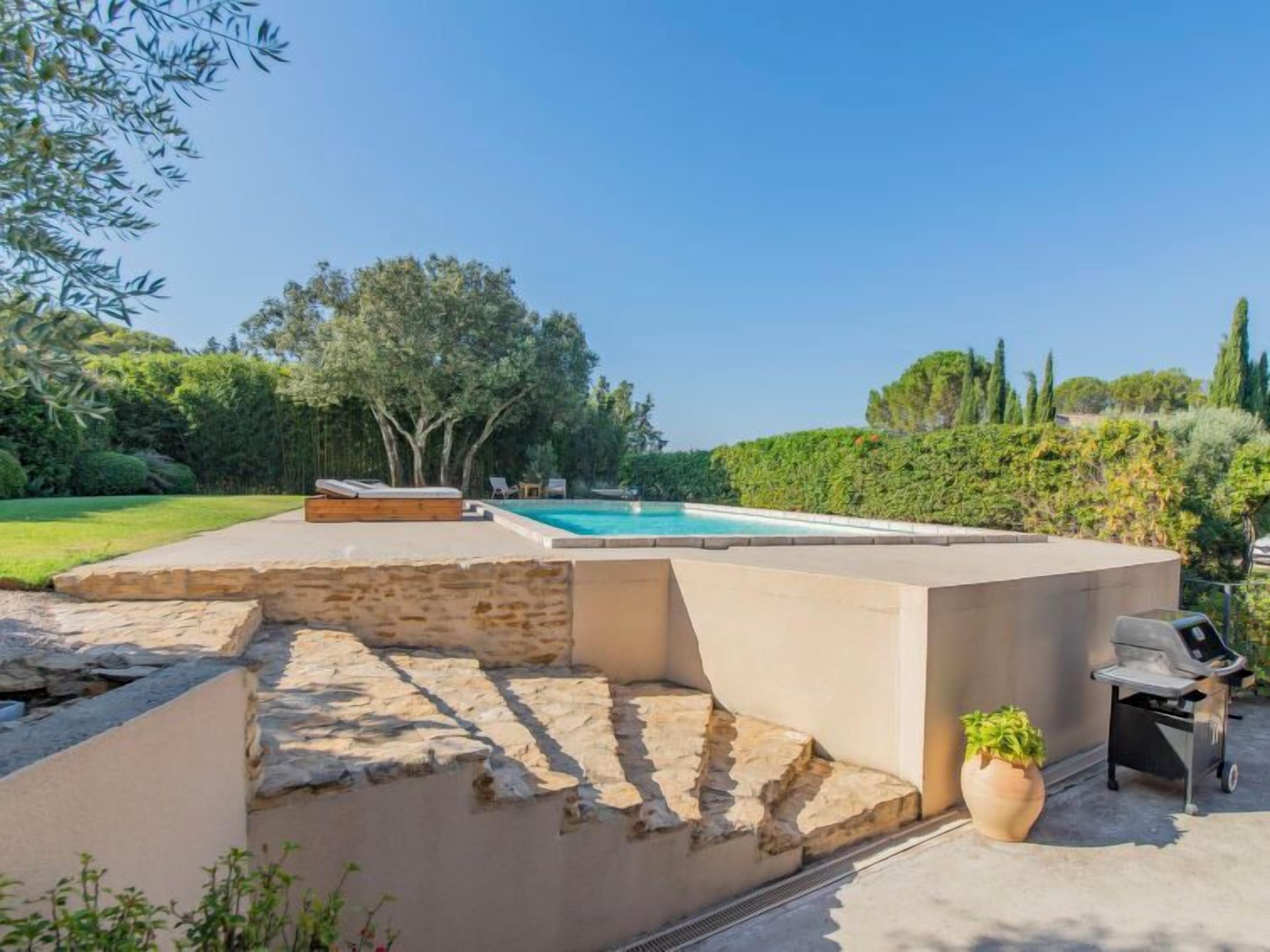 A pool area with stone steps leading to a lounge, surrounded by greenery and trees.
