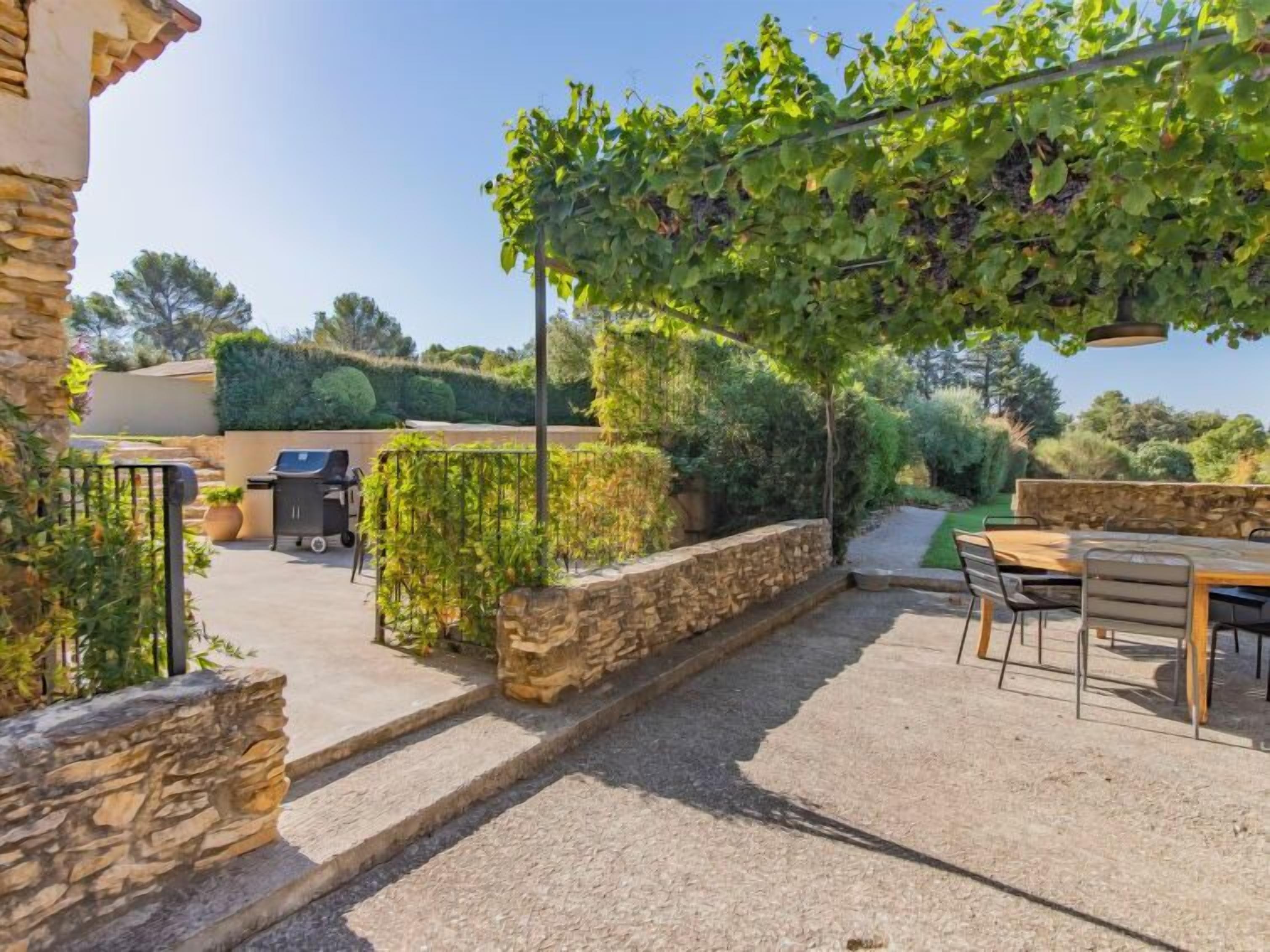 A patio area with a stone wall, a grill, and a table with chairs.