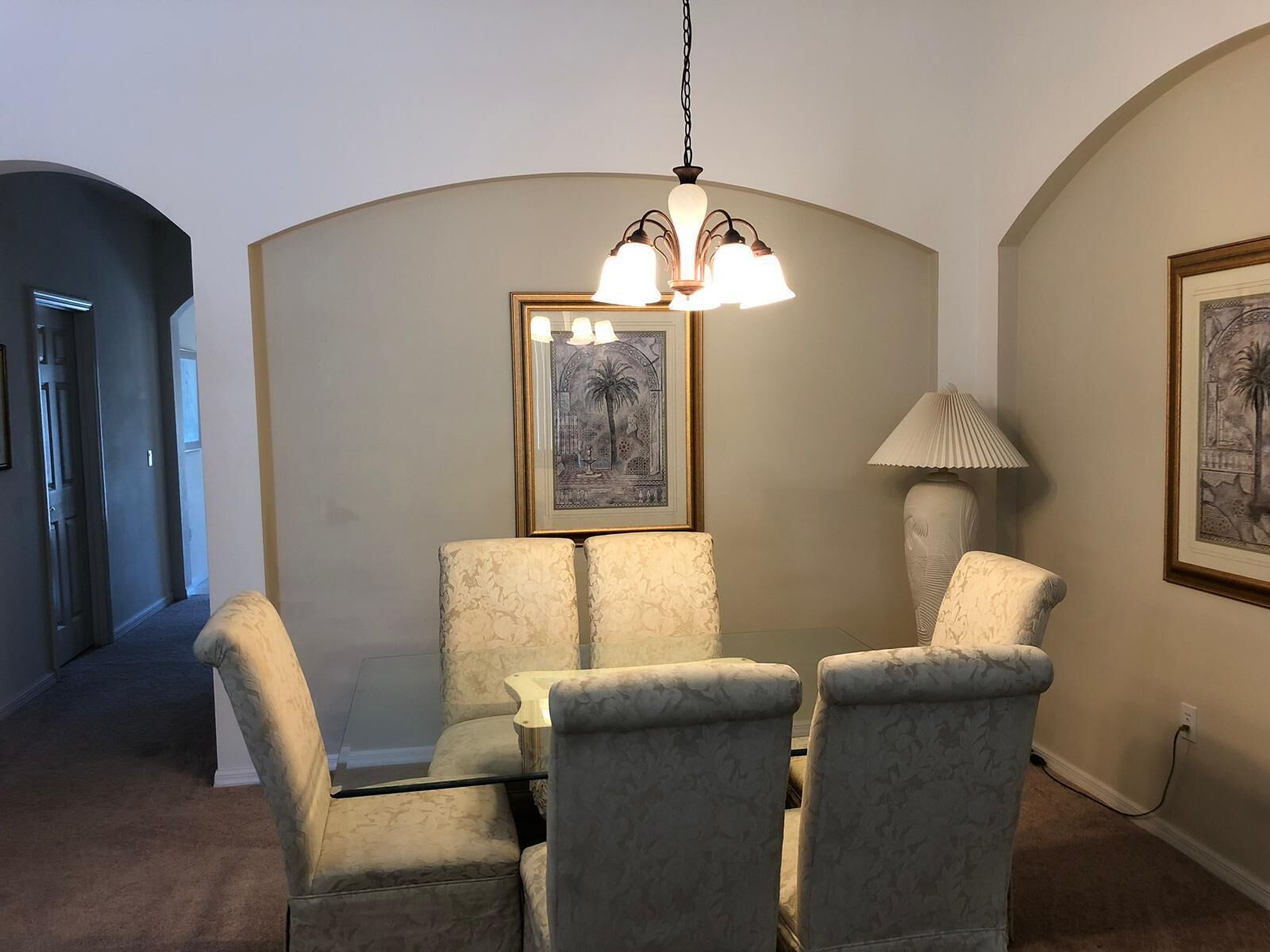 Un coin repas comprenant une table et quatre chaises, un lustre et deux tableaux encadrés accrochés aux murs.