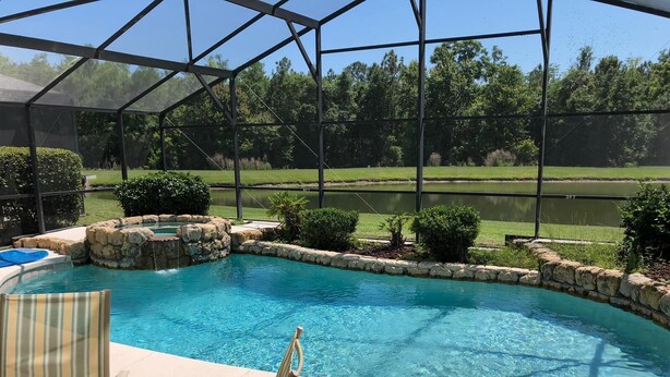 A pool with a stone border and a glass table and chair. - Relax with a lake view, pool and Jacuzzi (Kissimmee)