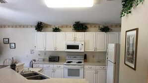 A kitchen with white cabinets, a microwave, a stove, and a refrigerator. - Relax with a lake view, pool and Jacuzzi (Kissimmee)
