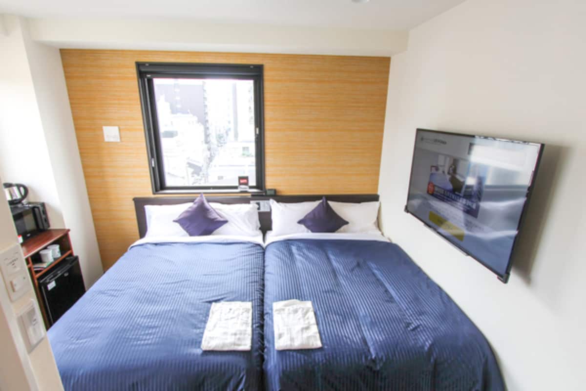 Una habitación de hotel con dos camas, un cabecero de madera, una ventana y un televisor en la pared.