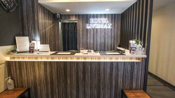 A hotel reception desk with a modern design, featuring a wooden panel backdrop and a sign that reads "HOTEL LIVINGMAX".
